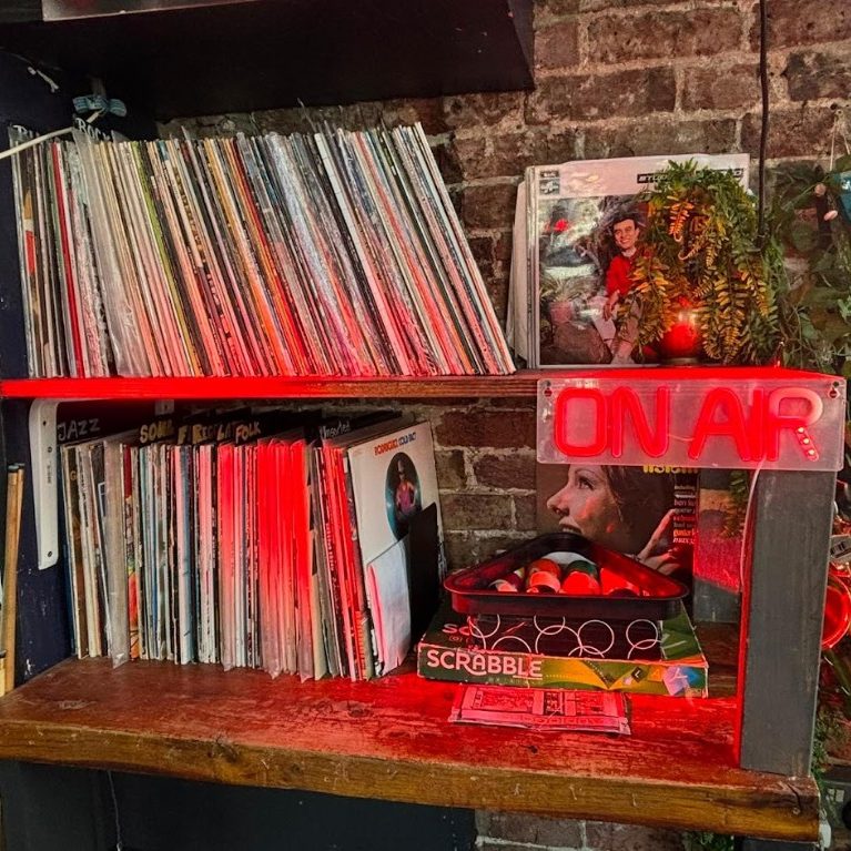 The record racks against bare brick, lit red by the ON AIR neon